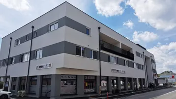 Modernes Geschäfts- und Wohngebäude mit weißer und grauer Fassade unter blauem Himmel.