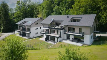 Moderne Mehrfamilienhäuser mit Balkonen und Terrassen, eingebettet in eine grüne Hügellandschaft.