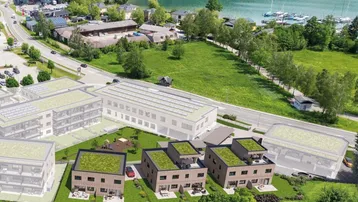 Luftaufnahme einer modernen Wohnanlage mit Gründächern und Photovoltaikanlagen am Seeufer.