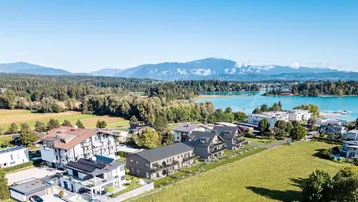 Luftaufnahme einer modernen Wohnanlage mit Seeblick und Bergpanorama in ländlicher Umgebung.