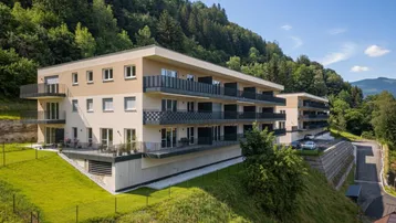 Modernes Apartmentgebäude am Hang mit Balkonen und Blick auf bewaldete Hügel.