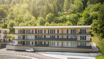 Modernes Apartmentgebäude mit mehreren Balkonen, umgeben von einem grünen Waldhang unter strahlendem Sonnenschein.