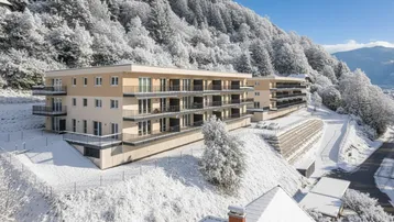 Die modernen Apartmentgebäude in einer verschneiten Winterlandschaft mit bewaldeten Hängen und weitem Bergblick.