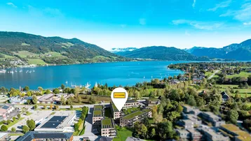 Luftaufnahme einer modernen Wohnanlage am See mit umliegender Berglandschaft und grünen Hügeln.