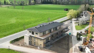 Neues Mehrfamilienhaus in ländlicher Umgebung mit Blick auf grüne Hügel und See, umgeben von Natur.