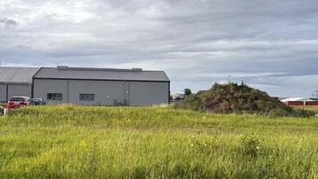Weitläufiges Grasfeld mit einem modernen Industriegebäude im Hintergrund unter bewölktem Himmel.