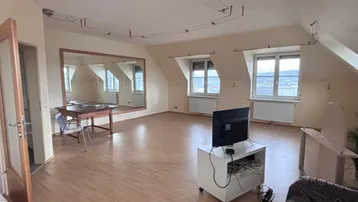 Geräumiges Wohnzimmer im Dachgeschoss mit Holzboden, großen Fenstern und einem großen Spiegel.