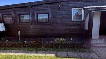 Dunkle Holzfassade eines Hauses mit kleinen Fenstern und einem gepflegten Vorgarten.