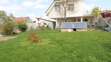 Großer Garten mit Rasenfläche und einem modernen Haus im Hintergrund, ausgestattet mit Solarpaneelen.