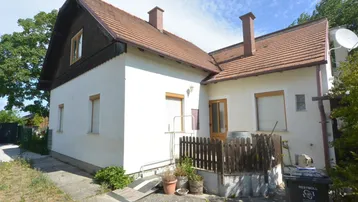 Seitenansicht des Hauses mit weißer Fassade, braunem Dach und kleinem Zaunbereich.
