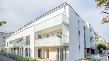 Modernes weißes Mehrfamilienhaus mit Balkonen und kleinen Terrassen im Erdgeschoss.