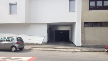 Eingang zur Tiefgarage eines modernen Wohngebäudes mit weißer Fassade und angrenzendem Altbau.