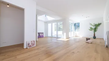 Helles, offenes Wohnzimmer mit Holzboden, großen Fenstern und viel Tageslicht.