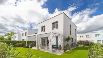 Modernes Einfamilienhaus mit gepflegtem Garten, Rasenfläche und überdachter Terrasse mit Pergola.