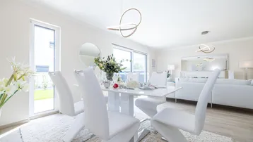 Eleganter Essbereich mit modernem weißen Tisch und Stühlen, viel Tageslicht durch große Fenster.
