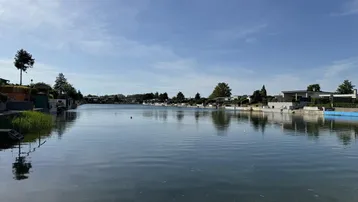Weiter Blick über einen ruhigen See mit Häusern am Ufer unter blauem Himmel.