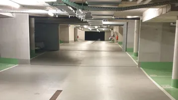 Geräumige Tiefgarage mit Betonstützen, sichtbaren Installationen an der Decke und markierten Parkplätzen.