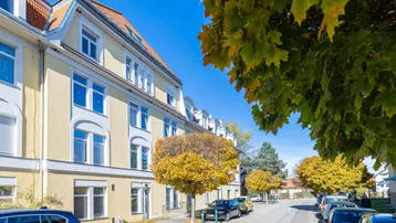 Attraktives Mehrfamilienhaus mit gelber Fassade und Bäumen in Herbstfarben.