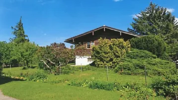 Charmantes Holzhaus umgeben von einem weitläufigen, gepflegten Garten mit altem Baumbestand unter blauem Himmel.