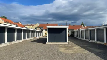 Reihen von modernen Garagen und eine freistehende Garage auf einem Schotterplatz unter bewölktem Himmel.