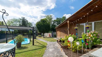 Holzhausfassade mit Blumenbeeten und einem Steinweg, der zum Pool im Garten führt.
