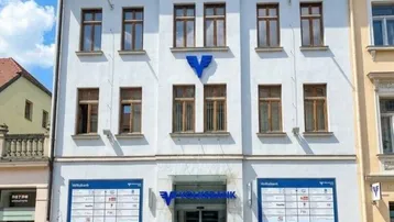 Historisches Gebäude mit weißer Fassade und braunen Fenstern an einer gepflasterten Straße.
