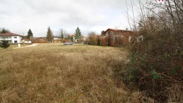 Ungenutztes Grundstück mit trockenem Gras und umliegenden Häusern unter bewölktem Himmel.