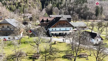 Luftaufnahme eines traditionellen Gebäudekomplexes mit mehreren Häusern, umgeben von einer weitläufigen Grünfläche und Bäumen.