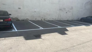 Mehrere markierte Außenparkplätze auf Asphaltfläche vor einer hellen Wand.