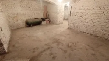 Geräumiger Kellerraum mit weiß gestrichenen Ziegelwänden, Betonboden und einem alten Tank.