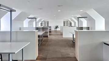 Großes, modernes Büro mit mehreren Arbeitsplätzen, Holzfußboden und schrägen Decken im Dachgeschoss.