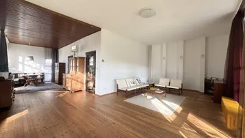 Geräumiger Wohn- und Essbereich mit Holzboden und Holzdecke, hell durch große Fenster.
