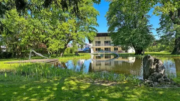 Großzügiger Gartenbereich mit Teich, Brücke und Spielplatz vor dem modernen Gebäude.