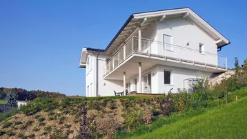 Weißes Einfamilienhaus auf einem Hügel mit Balkonen und weitem Blick in die Landschaft.