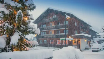 Traditionelles Gebäude im alpinen Stil, bedeckt mit frischem Schnee, umgeben von beleuchteten Bäumen.