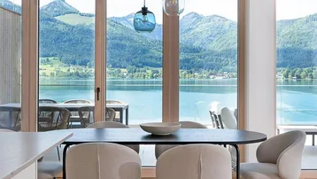 Moderner Essbereich mit Seeblick, großen Fenstern und stilvollen Pendelleuchten, ideal für gesellige Runden.