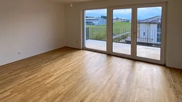 Helles Wohnzimmer mit neuem Parkettboden und Zugang zu einem Balkon mit Blick ins Grüne.