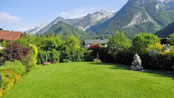 Gepflegter Garten mit weitläufiger Rasenfläche und beeindruckendem Bergblick im Hintergrund.