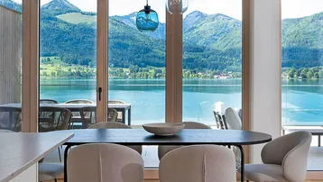 Moderner Essbereich mit Seeblick und Bergblick durch große Fenster, ergänzt durch stilvolle Pendelleuchten.