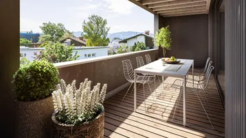 Geräumiger Balkon mit Holzboden, Esstisch und Blick auf die umliegende Landschaft und Berge.