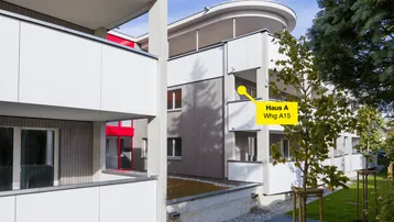 Moderne Wohngebäude mit Balkonen, Holzfassade und begrünten Außenbereichen unter blauem Himmel.