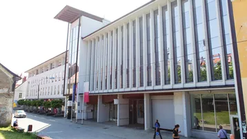 Modernes Gebäude mit großer Glasfassade und vertikalen Lamellen an einer belebten Straße.