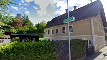 Ansicht des Gebäudes von der Straße mit einem Straßenschild und grüner Hecke.