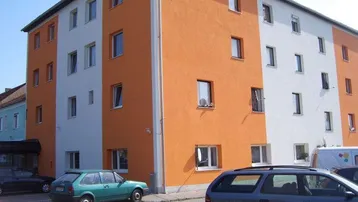 Mehrfamilienhaus mit orangefarbener und weißer Fassade sowie geparkten Autos davor.