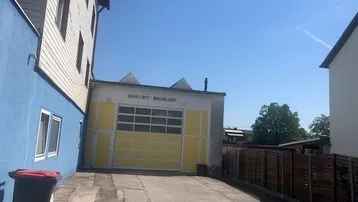 Außenansicht eines Gebäudes mit großer gelber Garagentür und blauer Fassade unter klarem Himmel.