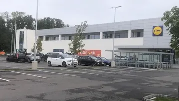Außenansicht eines modernen Lidl-Supermarktes mit großem Parkplatz unter bewölktem Himmel.