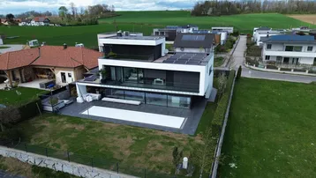 Moderne Villa mit Flachdach, Solarpaneelen und einem Pool, umgeben von grünen Feldern.