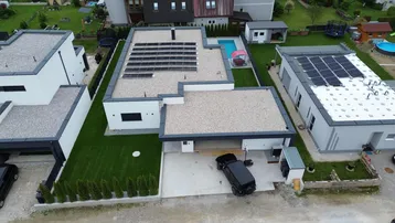 Luftaufnahme eines modernen Neubaus mit Flachdach, Photovoltaikanlage, Pool und gepflegtem Garten in ländlicher Umgebung.
