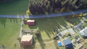 Luftaufnahme einer ländlichen Gegend mit Häusern, einer Straße und dichtem Wald im Hintergrund.