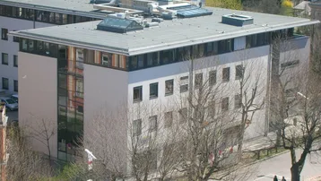 Moderne Gebäudearchitektur von oben mit Flachdach, vielen Fenstern und umliegender Vegetation.